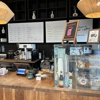 Forth & Nomad - The photo depicts the interior of Café Forth, featuring a wooden counter, digital menu screens, baked goods in a display case, and coffee-making equipment. - Accessories Near Me - Houston, Texas