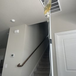 An IV drip is attached to a stand positioned next to a staircase in a home interior, with a ceiling vent visible.