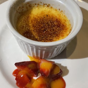 Amaya - A dessert presentation includes a ramekin of crème brûlée with a caramelized sugar crust on top, placed on a white plate. Next to it are strawberries coated with a yellow sauce, likely a fruit or custard sauce. The setting appears to be in a restaurant or dining environment. - New American Near Me - Santa Fe, New Mexico