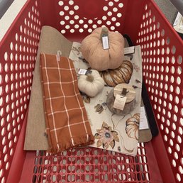 Fall decor - A red shopping cart holds fall decor items such as fabric pumpkins, a floral rug, a plaid scarf, and a candle.