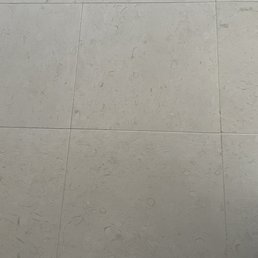Grouted Limestone Tile 24x24 - A photograph of a tiled floor featuring large, light gray tiles with a textured surface and subtle pattern, likely in an indoor setting.