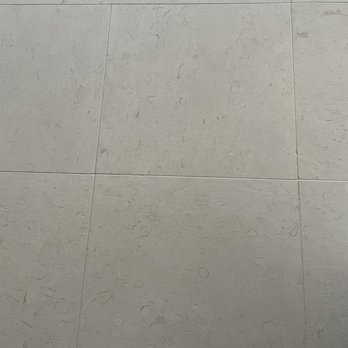 Strusis Tile Installations - Grouted Limestone Tile 24x24 - A photograph of a tiled floor featuring large, light gray tiles with a textured surface and subtle pattern, likely in an indoor setting. - Tiling Near Me - Chino, California