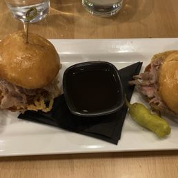 Prime rib sliders - A plate with two prime rib sliders, a pickle, and a small container of dipping sauce, served at Boulder Social in Boulder, Colorado.