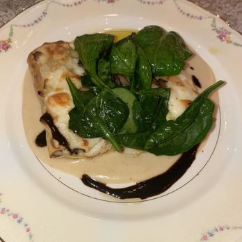 Hidden Creek Estates - a plate of food with spinach - A serving of lasagna with melted cheese, topped with fresh spinach leaves, served on a decorative floral plate with sauce around it. - Venues & Event Spaces Near Me - Roscoe, Illinois