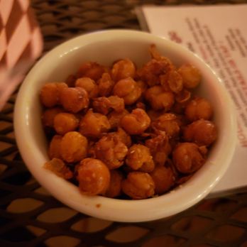 Vesper Lounge - Moroccan Bar Nuts - A white bowl contains roasted chickpeas, placed on a dark, textured table surface, with a menu partially visible in the background. - Bars Near Me - Denver, Colorado