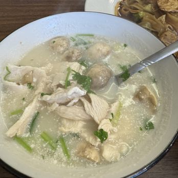 Jo Wok - A bowl of chicken and meatball soup garnished with chopped green onions, served on a wooden table with a side plate of noodles. - Thai Near Me - Sandusky, Ohio