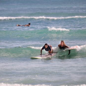 Kahu Surf School - Kyle pushing Jolene onto the wave - Surf Schools Near Me - Honolulu, Hawaii