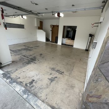 Epoxy Time - Before - A spacious garage with a stained concrete floor, white walls, and a partially open garage door, showing some interior features and equipment. - Flooring Near Me - Riverside, California