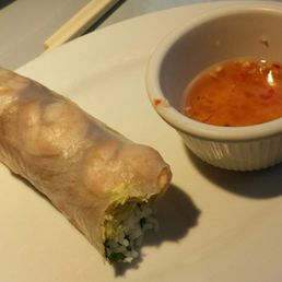 Shrimp spring rolls, seafood showing side. - A Vietnamese spring roll with translucent rice paper, filled with vegetables and rice noodles, served with a small bowl of dipping sauce.