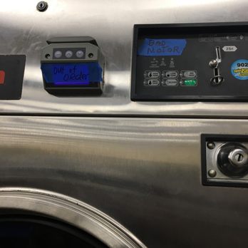 SpinZone Laundry - A stainless steel laundry machine features handwritten notes on blue tape, with one label reading 'BAD MOTOR' and another stating 'OUT of order.' The machine has control panels and a coin slot, indicating it is part of a coin-operated laundry facility. The notes suggest the machine is currently non-functional due to mechanical issues. - Laundromat Near Me - Austin, Texas