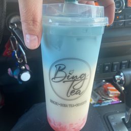 Imperial Jasmine Tea - A person holds a large boba tea cup with a gradient of pink, yellow, and blue colors, inside a vehicle with visible dashboard elements.