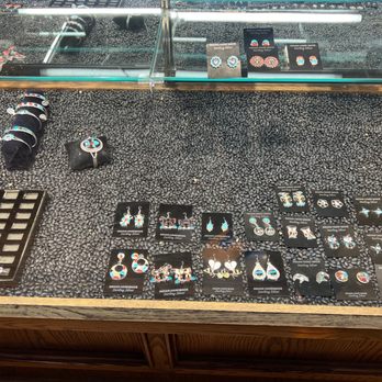 Covered Wagon - A jewelry display case features handcrafted silver jewelry, including earrings, bracelets, and rings. Items are arranged on black display cards and small cushions, with some jewelry featuring colorful accents. The case has a glass top and a wooden base, with additional jewelry pieces and display cards visible inside the case. - Jewelry Near Me - Albuquerque, New Mexico