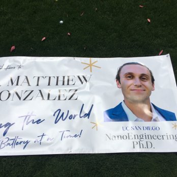 MAC Printing - A printed banner celebrating Dr. Matthew Gonzalez, a UC San Diego NanoEngineering Ph.D., is laid on grass with scattered flower petals. - Printing Services Near Me - La Mesa, California