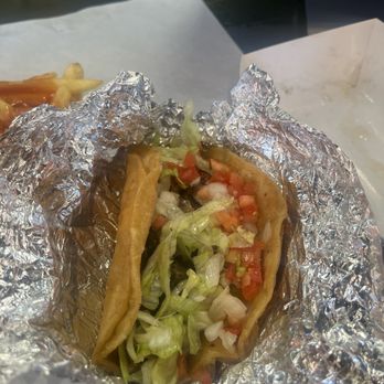 Peeples Taco’s - Taco - A taco filled with lettuce, diced tomatoes, and other ingredients, wrapped in aluminum foil, on a piece of white paper. - Fast Food Near Me - Hazel Crest, Illinois
