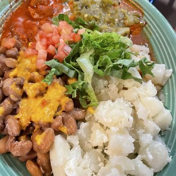 Duran Central Pharmacy - Adovada - A plate contains baked beans topped with melted cheese, diced tomatoes, shredded lettuce, mashed potatoes, and two types of sauces—green and red—likely served as part of a Mexican dish. The food is arranged on a green plate, with the sauces placed at the top, and the vegetables and beans filling the remaining space. - Mexican Near Me - Albuquerque, New Mexico