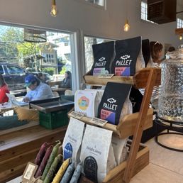 Beans and local artisan goods to buy. Slight view of outdoor seating and warm ambiance within.