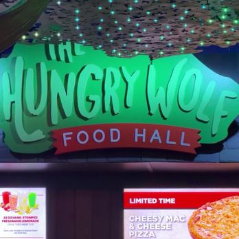 Great Wolf Lodge - Hungry wolf food Hall - A large illuminated sign reads 'The Hungry Wolf Food Hall' with stylized green and red lettering. Below the sign, a digital menu screen displays food options, including a cheesy mac and cheese pizza with prices. The ceiling above has decorative elements resembling clouds with small, glowing lights, creating a themed atmosphere. - Resorts Near Me - Mashantucket, Connecticut