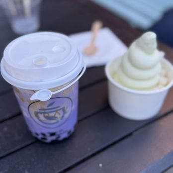 Krav Cafe - Dirty ube latte with boba and cheese cap, a joke of a "matcha" soft serve - A purple ube latte with boba and a white lid is placed on a dark outdoor table, alongside a cup of vanilla soft serve ice cream. - Cafes Near Me - Denver, Colorado