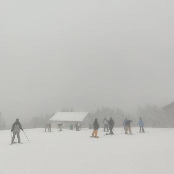 Mount Snow - People are skiing and snowboarding on a snow-covered slope with foggy conditions, and small buildings are visible in the background. - Ski Resorts Near Me - West Dover, Vermont