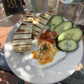 Coronet Cafe - Çilbir plate - A dish featuring grilled bread, sliced cucumbers, cherry tomatoes, and a poached egg on a bed of yogurt or sauce, served outdoors. - Cafes Near Me - Tucson, Arizona