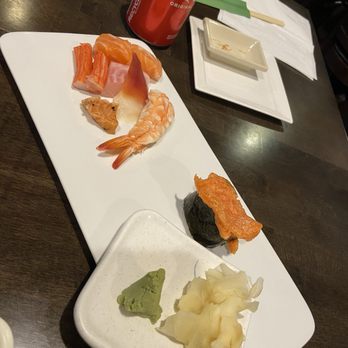 Sushi Palace - Assorted sashimi - A white rectangular platter holds various sushi and sashimi pieces, accompanied by wasabi and pickled ginger. A Coca-Cola can is placed behind the platter on a dark wooden table. - Sushi Bars Near Me - Summit, New Jersey