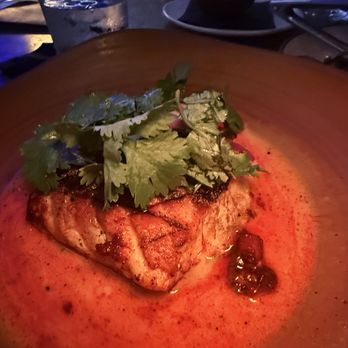 Bulevar Mexican Kitchen - Snapper. Yum. - A grilled fish fillet topped with cilantro is served on a plate with a reddish sauce and some dark condiments, in a dimly lit restaurant setting. - Mexican Near Me - Austin, Texas