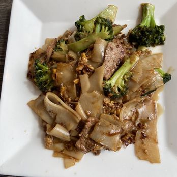 Pinto Thai Kitchen - Pad See Eiw Lunch Special with beef - A square white plate contains Pad See Eiw with broccoli, beef, and wide rice noodles, served on a dark wooden table. - Thai Near Me - Evanston, Illinois
