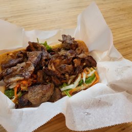 Grilled Pork Banh Mi - A banh mi sandwich with grilled pork, vegetables, and herbs served on a paper-lined tray.