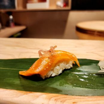 Roji - salmon - Salmon sushi with a garnish on a green leaf, served on a wooden plate in a Japanese restaurant setting. - Sushi Bars Near Me - Cincinnati, Ohio