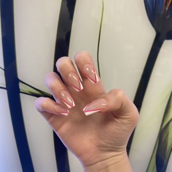 Cobblestone Spa & Nails - Design Prom Nails! - A close-up of a hand displaying manicured nails with a clear base and red and white geometric nail art, set against a decorative background. - Nail Salons Near Me - Tempe, Arizona