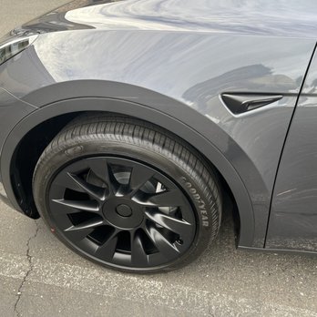 Ceramic Garage - The image shows the front left side of a gray Tesla car, focusing on the wheel and fender, parked on asphalt. - Car Window Tinting Near Me - Modesto, California