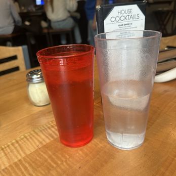 Vendetta's Restaurant - Someone else's water definitely delivered to my table - A red-colored drink and a glass of water are placed on a wooden table in a restaurant setting, with a menu for house cocktails visible. - Italian Near Me - Vail, Colorado
