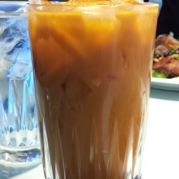 Cafe Da Lat - Thai ice tea. Big glass. Typical taste, which is to say sweet & mildly spiced. - A tall glass filled with Thai iced tea, ice cubes, and a straw, placed on a table in a restaurant setting. - Vietnamese Near Me - Albuquerque, New Mexico