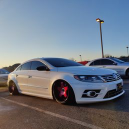20 percent on windshield - A white Volkswagen sedan with tinted windows and pink custom wheels is parked in a parking lot at sunset, with other cars nearby.