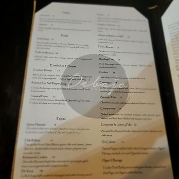 Debajo Tapas ABQ - Seasonal menu - A menu from a restaurant offering Spanish-inspired cuisine, including salads, soups, and tapas. The menu lists dishes such as Paella, Ensaladas & Sopas, and various tapas like Queso Plameado and Ceviche. Prices are indicated next to each item, and the menu is printed on white paper with a simple layout. The background surface is dark, and the menu is slightly angled. - Spanish Near Me - Albuquerque, New Mexico