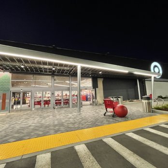 Target - Loving what they did outside - Exterior view of a Target store at night, showing the entrance with glass doors, shopping carts, and outdoor decor including large red spheres. - Department Stores Near Me - Cupertino, California