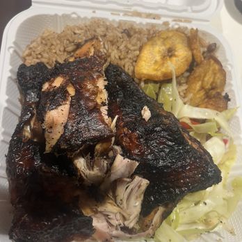 Wadadli - A takeout box contains grilled fish with charred skin, rice, fried plantains, and a side of cooked vegetables. - Caribbean Near Me - Brooklyn, New York