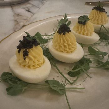 The Franklin - Deviled eggs - Four deviled eggs with piped yellow filling, topped with black caviar and a small green leaf, arranged on a plate with greenery. - Cocktail Bars Near Me - Bristol, Rhode Island