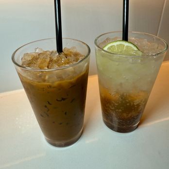 Phoxotic - Vietnamese Coffee & Plum Soda - Two iced beverages in tall glasses are placed on a white surface, one with a lime wedge and the other with a black straw, likely at a restaurant or cafe. - Vietnamese Near Me - Washington, DC, District of Columbia