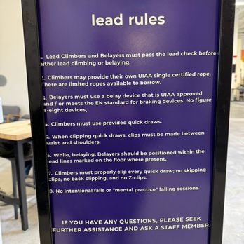 Movement Centennial - Lead climbing rules. Some of these probably don't matter once you have your belay card. I did see people taking intentional falls on lead. - A vertical sign with a purple background and white text outlines lead climbing rules at a climbing gym. The rules cover belaying, rope use, device standards, quick draws, and safety practices. The sign provides instructions for climbers and belayers to ensure safety during lead climbing activities. - Rock Climbing Near Me - Centennial, Colorado