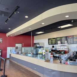 Interior of a poke restaurant featuring a curved counter, glass display, and menu boards on the wall, with a staff member behind the counter.