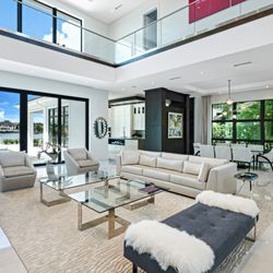 Integrative Designs - Expansive living room with soaring ceilings, sleek furnishings, and floor-to-ceiling windows opening to waterfront views.
