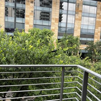 Violet Crown Austin - A balcony with metal railing overlooks green trees and a modern glass building with stone accents. - Cinema Near Me - Austin, Texas