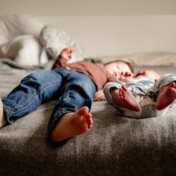 The Enloe Creative - Toddler and infant brother lay on bed with matching little pairs of feet towards the camera.
