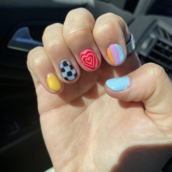 Nuvé - Nails done by Trinity - A person's hand with decorated nails featuring various colorful designs, including hearts, checks, and abstract patterns, is shown inside a vehicle. - Hair Salons Near Me - Albuquerque, New Mexico