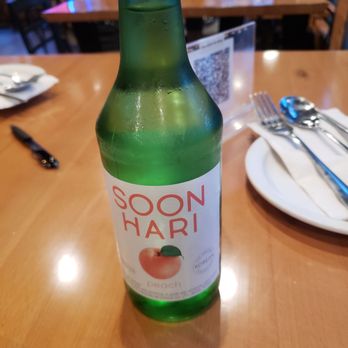 SoJu BBQ - A green glass bottle labeled SOON HARI peach is placed on a wooden restaurant table, with a plate, utensils, and a QR code in the background. - Korean Near Me - Chicago, Illinois