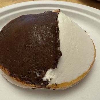 Modern Pastry Shop - Black and White Cookie - A cookie with half chocolate frosting and half vanilla frosting, placed on a white plate, with a wooden table in the background. - Bakeries Near Me - Boston, Massachusetts