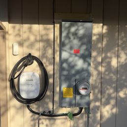 200 amp panel upgrade and EV charger! - An electrical panel and an EV charger are mounted on an exterior wall, with shadows of trees cast on the wall.