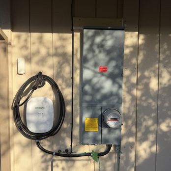 Connected Technology - 200 amp panel upgrade and EV charger! - An electrical panel and an EV charger are mounted on an exterior wall, with shadows of trees cast on the wall. - Electricians Near Me - Rocklin, California