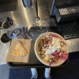 my bowl with a pita bread - A tray holds a salad with cheese and vegetables, a slice of pita bread, and a glass of water on a counter at a restaurant or cafe.